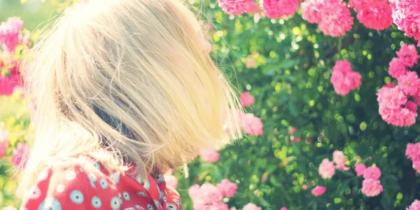 A blonde haired girl in a red dress is by some pink flowers